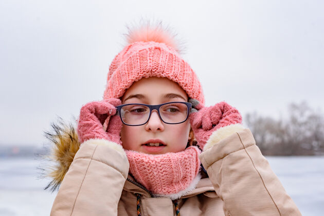 微笑戴着粉色帽子和外套的少女站在冬天的风景中冬天的孩子画像肖像季节自然