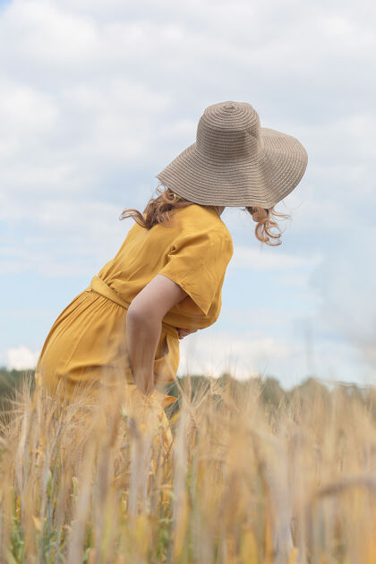 肥料在一个阳光明媚的夏日 一位年轻漂亮的孕妇穿着黄色的裙子 戴着黄色的帽子 走过一片麦田出生模糊阳光