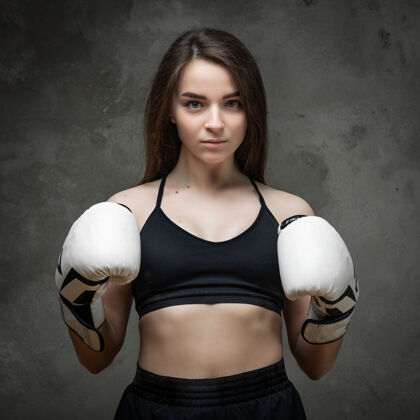 女子一个穿着短上衣和拳击手套的年轻运动型女子拳击手的肖像把他的手放在架子上 在深灰色的背景上摆姿势能量运动训练