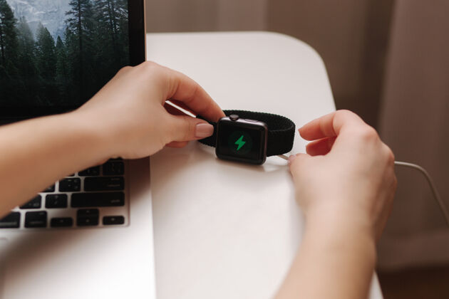 电缆女性手把智能手表无线充电与屏幕上的充电指示灯工作地点靠近笔记本电脑设备设备桌子
