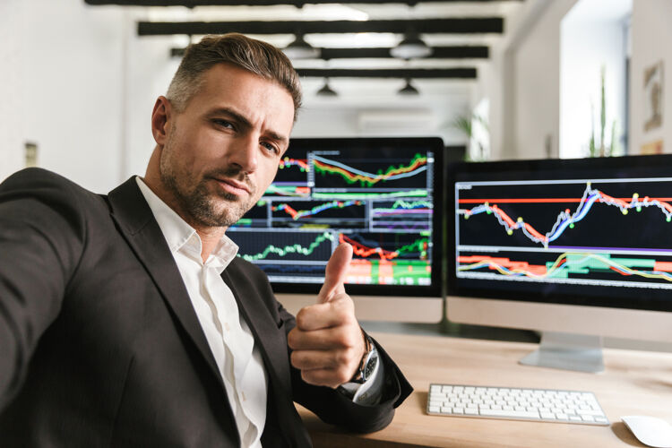 西装一张30多岁的自信男人穿着西装在办公室里用电脑自拍的照片 屏幕上有图片和图表工作员工数据