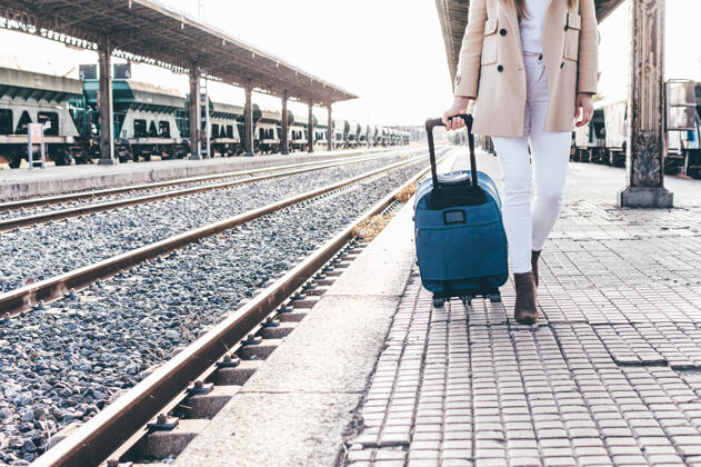 火车一个穿着贝雷帽和米色夹克的女孩带着手提箱穿过火车站的画像交通女孩城市