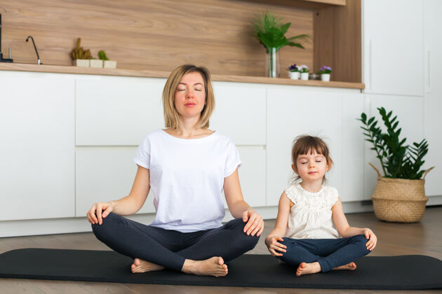 内心的快乐女人和她可爱的小女儿坐在莲花的位置 而在家里一起做瑜伽活动训练女孩