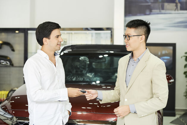 司机年轻的商人站在汽车陈列室里 从亚洲推销员那里得到一把新车的钥匙汽车男人客户