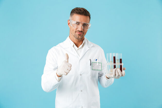 男人年轻的医生戴着眼镜拿着带血的试管 孤零零地站在蓝色的墙上治疗医疗中年