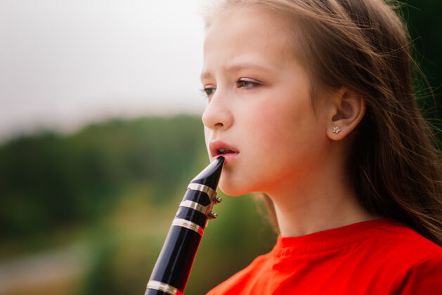 公园年轻漂亮的女孩吹单簧管 秋天公园里的乌木乐器表演娱乐