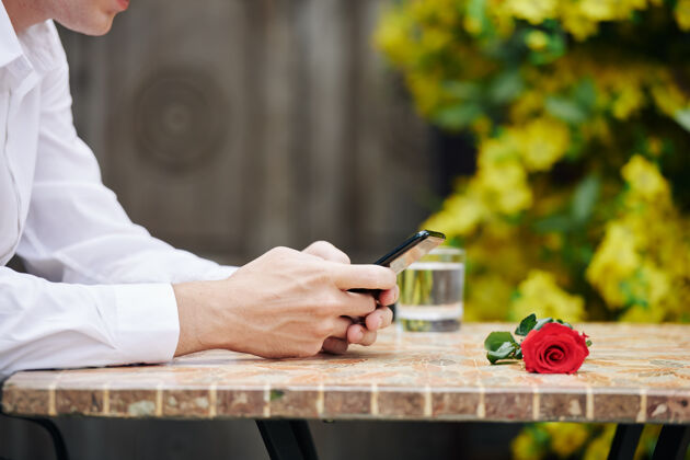 无线技术一个年轻人坐在户外咖啡馆里等待约会时给朋友发短信的剪贴图片使用电话手机打字