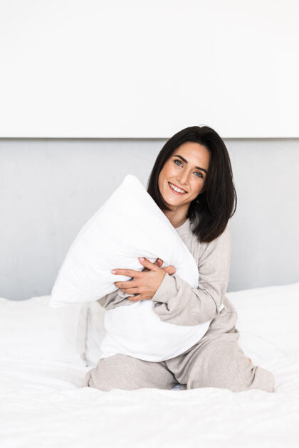肖像快乐的女人30多岁的形象笑 而在床上玩在家里的枕头乐趣谎言床白种人