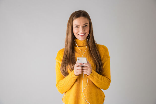 白种人一个美丽快乐的年轻女子用手机隔着灰色的墙被孤立的画面手机毛衣黑发