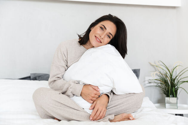 吸引30多岁的成年女子坐在床上 枕着白色枕头 在家休息的肖像室内快乐公寓