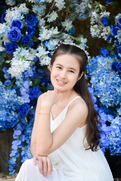 快乐美丽的亚洲女人穿着白色的裙子坐在蓝色的花前年轻新鲜可爱