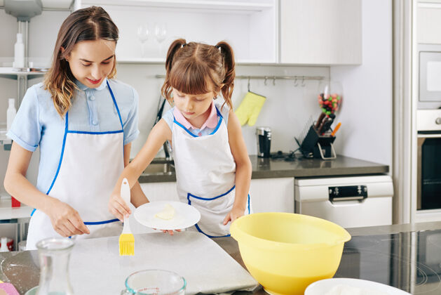 鸡蛋年轻的妈妈在羊皮纸上涂黄油的时候用硅胶刷看着小女孩烘焙单快乐女人