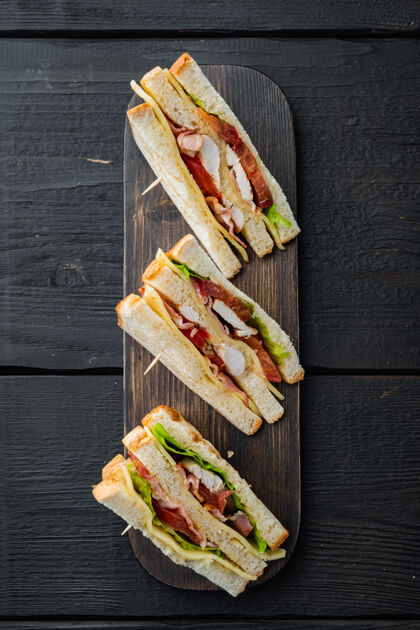 火腿自制的俱乐部三明治 用火鸡 培根 火腿 西红柿做成 放在黑木桌上 俯视图健康木桌西红柿