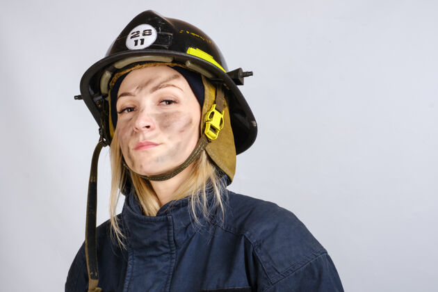 女人穿制服的年轻勇敢的女人的近距离的脸 消防员的安全帽l头盔严肃安全帽