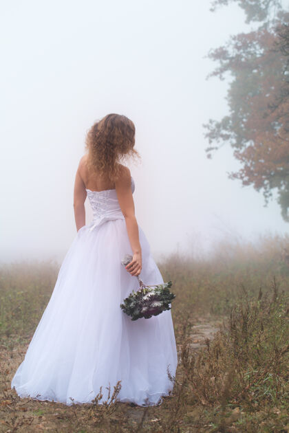 新娘美丽的新娘 带着一束花束 背景是雾蒙蒙的田野雾新娘花