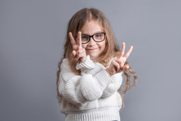 可爱一个年轻漂亮的金发小女孩的肖像 穿着毛衣 上面有v字标志胜利女人手指