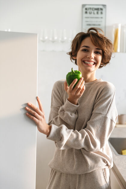 漂亮微笑的年轻女子站在冰箱旁 手里拿着苹果年轻吸引力膳食