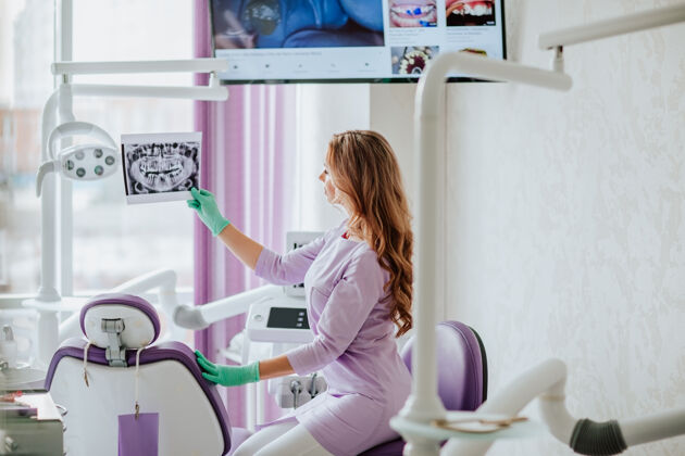 医院年轻迷人的牙医的肖像 长卷发 穿着紫色的医疗制服 戴着绿色的医疗手套 在柜子里摆着x光照片个人卫生牙痛