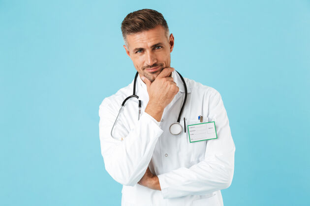 男人身着白色制服 手持听诊器的快乐医生的画像 孤立地站在蓝色的墙上肖像微笑外套