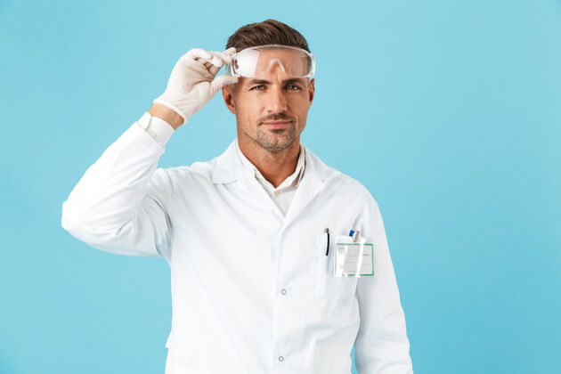 肖像自信的男医生穿着制服戴着眼镜孤立地站在蓝色的墙上吸引力医生实验室