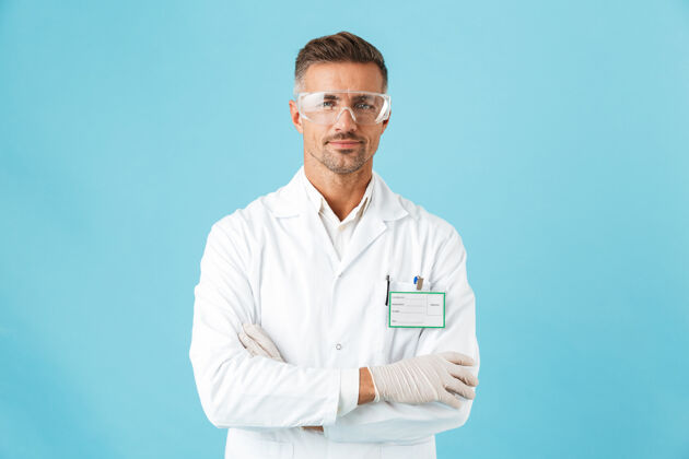 保护自信的男医生穿着制服戴着眼镜孤立地站在蓝色的墙上医学外套从业者
