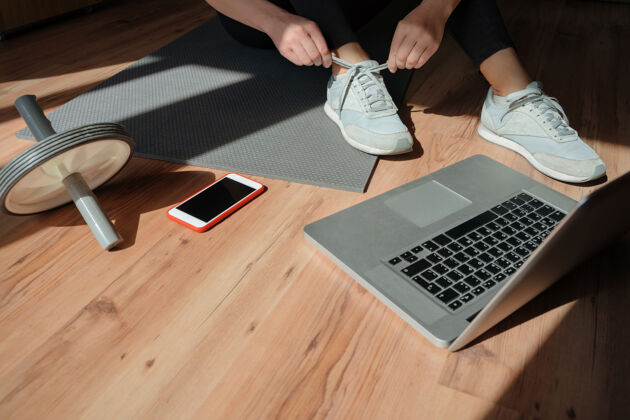 健康一位运动型女士坐在客厅的地板上 用笔记本电脑在家里进行在线锻炼普拉提体操地毯