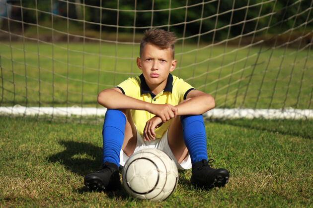 比赛穿着黄色t恤的帅哥足球运动员拿着球坐在球门附近竞争孩子足球