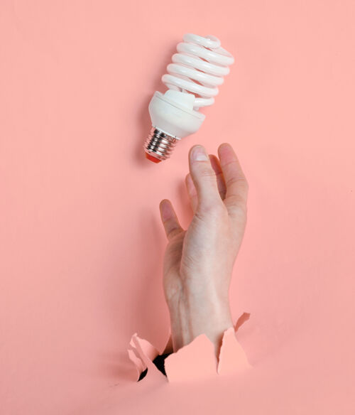 手臂女性手拿着螺旋灯泡穿过撕破的粉红色纸简约创意时尚理念灯能源环境