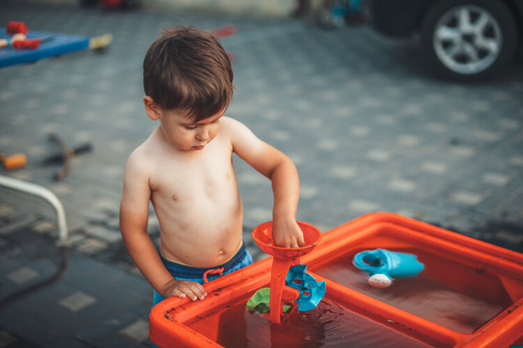 欢呼一个没穿衣服的可爱男孩在院子里玩水和塑料玩具集中兄弟魅力