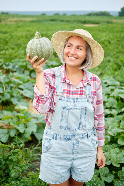 食物在植物上拿着新鲜绿色南瓜的女人田野美丽在阳光明媚的温暖天气里 一个拿着健康蔬菜食品的小女孩站在农场上日间栽培纯素文化有机自然产品吃栽培女性