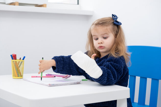 童年坐在桌边用马克笔试着画画的小女孩手拿石膏标记矫形医学