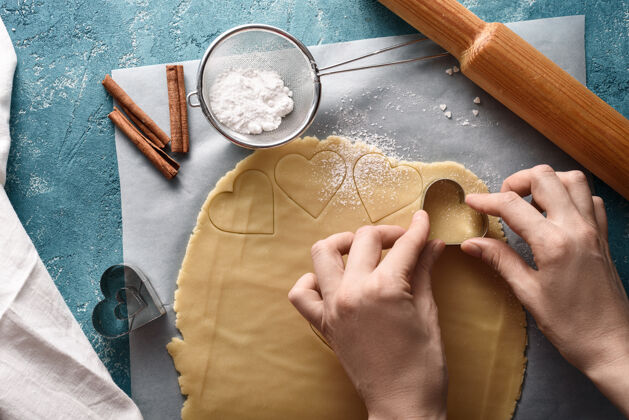 酥饼用厨房配件在蓝色背景上的饼干面团上塑造心形的过程俯视图手毛巾烹饪