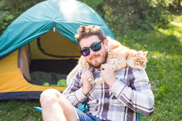 游客戴墨镜的男人把猫扛在肩上美丽旅游露营地