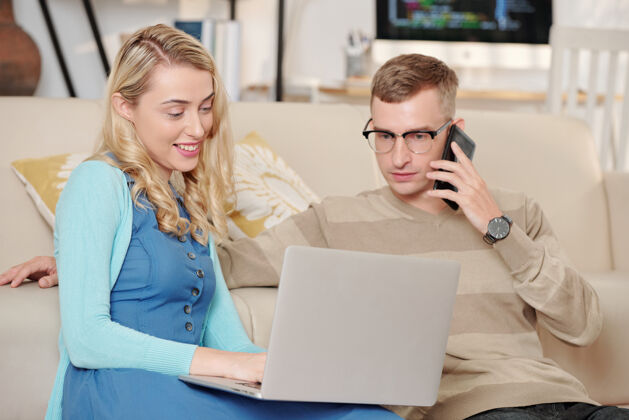 技术漂亮的年轻女子在笔记本电脑屏幕上向正在打电话的丈夫展示一些有趣的东西讨论通话关系