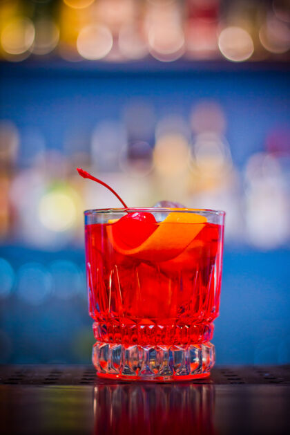 鸡尾酒内格罗尼红在玻璃瓶中饮用带有樱桃和橘皮的鸡尾酒甜的玻璃杯美式