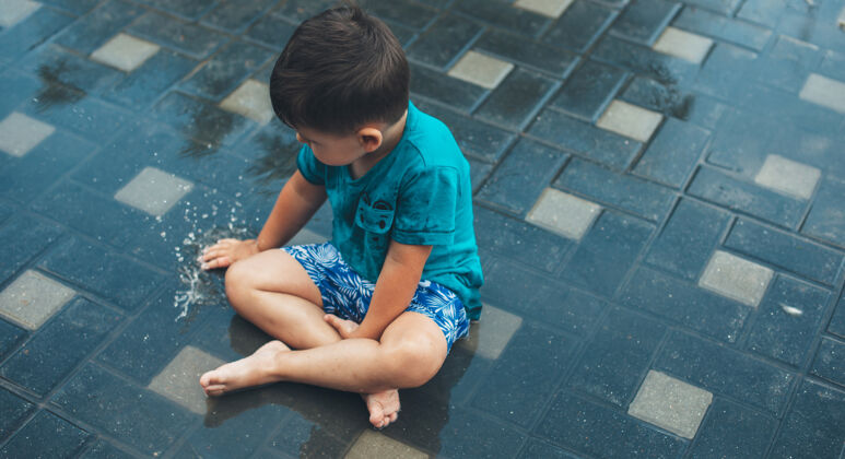 滴上图是一个白人男孩雨后在地上玩水的照片孩子自然水坑