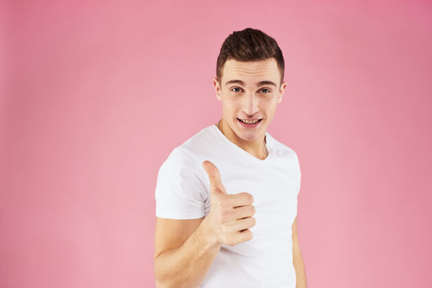 年轻一个穿着白色t恤衫的男人用他的手示意着粉色工作室的剪影男人手指欢呼
