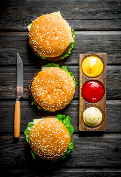 番茄酱黑木桌上放着不同酱汁的汉堡和一把刀番茄午餐绿色
