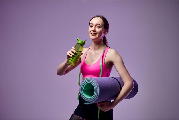 健康的生活方式穿着运动服的运动美女 手里拿着一瓶水和一张紫色的健身垫去健身房吧哑铃运动装健康