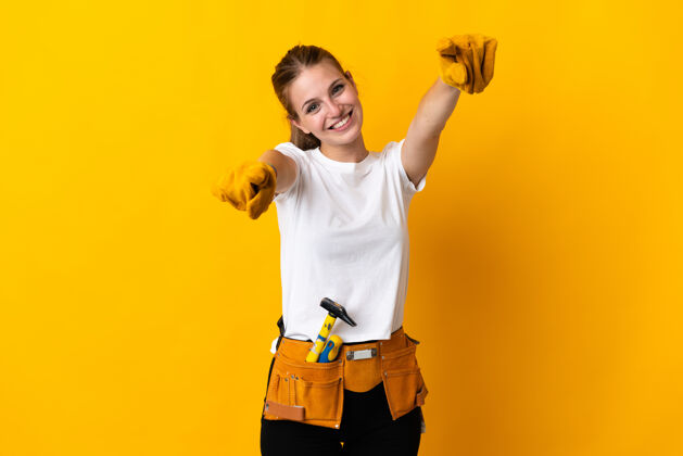 工人被隔离在黄色背景上的年轻电工女士微笑着指着你女孩木匠时尚