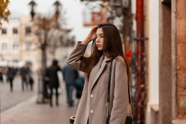 时尚一个穿着时髦灰色外套的欧洲年轻女子在一个秋天的城市的街道上年轻户外手提包