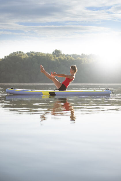 快乐日出时在划桨板上练习瑜伽的女人美丽锻炼练习