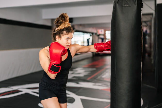 打击女子拳击手训练与红色拳击手套直接打到一个拳击袋在健身房肌肉女人女人