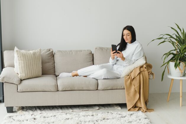 女孩一个快乐的年轻女子在家里的沙发上休息时使用手机的画像快乐人移动