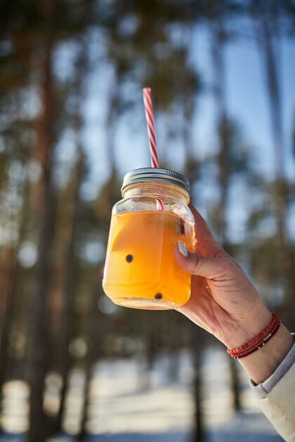 酒精冬天的森林里 女人的手拿着一杯熟酒马克杯冬天森林