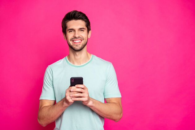 网络照片中的博主手里拿着电话检查订阅者牙牙学语微笑着穿休闲装孤立生动的粉红色背景男人手机浏览