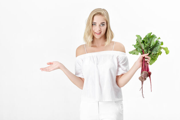 维生素一位穿着白色上衣的金发美女手持一根长着绿叶的甜菜根背景.健康还有维生素烹饪自然举行