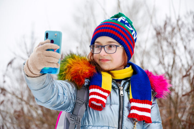 寒冷冬日少女的画像在她的温暖服装.青少年女孩在智能手机上自拍围巾女孩青少年