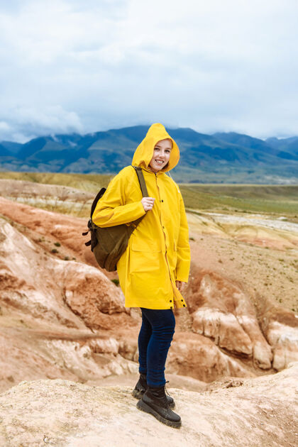人类穿着黄色雨衣背着背包的微笑的徒步女孩年轻人人远足者