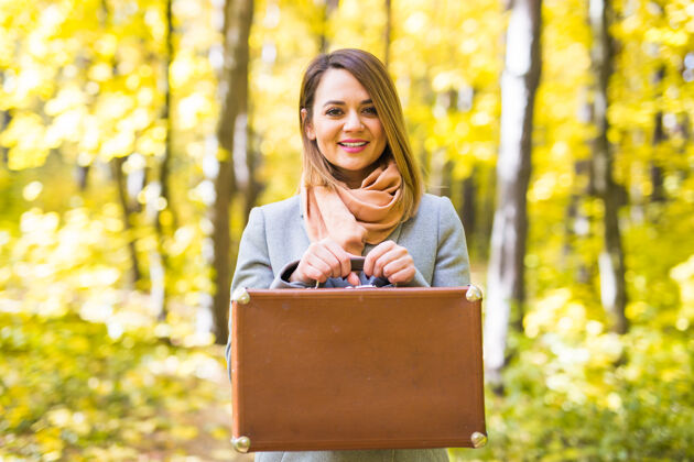 20岁秋天 季节和人的概念-迷人的女人站在公园复古手提箱在秋天快乐森林季节